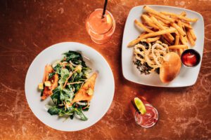 overhead photo of crispy rice salad, truffle mushroom burger and cocktails